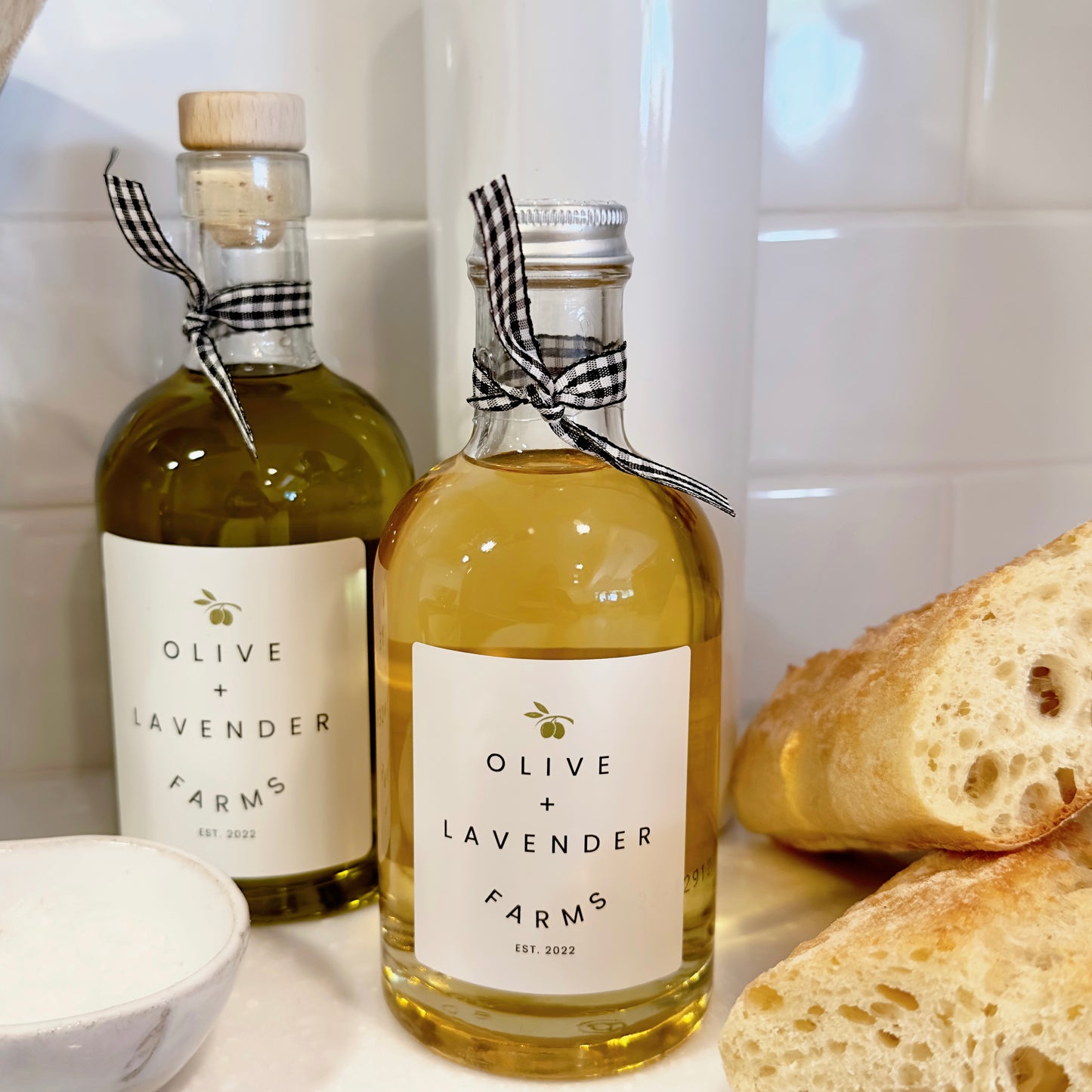 A bottle of white balsamic vinegar and olive oil from Olive & Lavender Farms with bread on a kitchen counter.