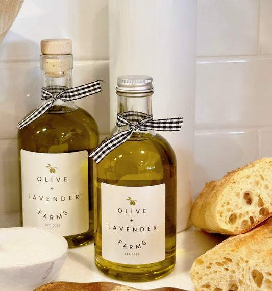 Two bottles of Olive + Lavender Farms olive oil with bread on a kitchen counter.