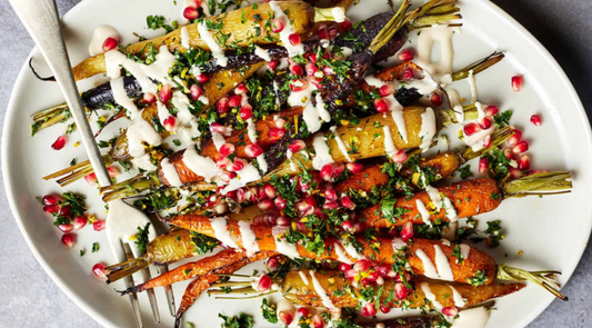 Roasted carrots on a serving dish with drizzle of tahini and pomegranate seeds 