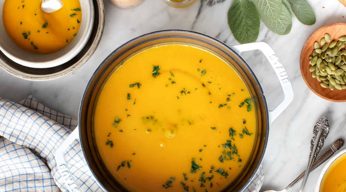 Orange colored soup in white ramekin on kitchen counter