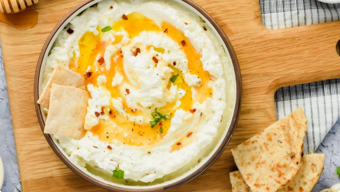 white creamy dip in large bowl with pita chips and orange oil on top.