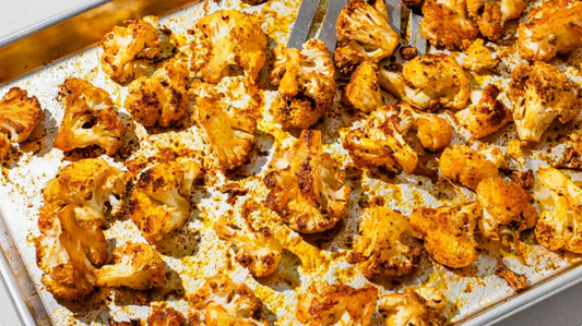 Charred and orange-hued cauliflower florets on a baking sheet
