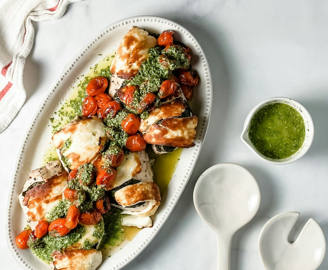 Chicken breast on a large white platter topped with herb vinaigrette and blistered tomatoes