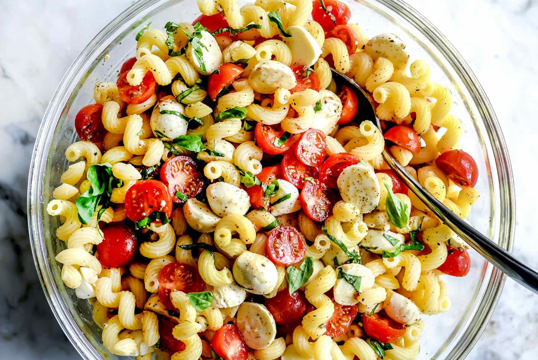 Pasta with tomatoes, mozzarella and basil in a glass bowl on a white countertop